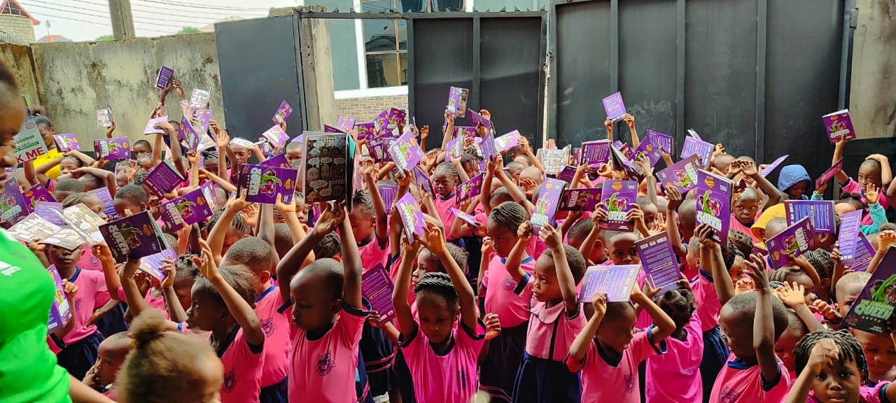 A large school outreach scene with children lifting their copies together.